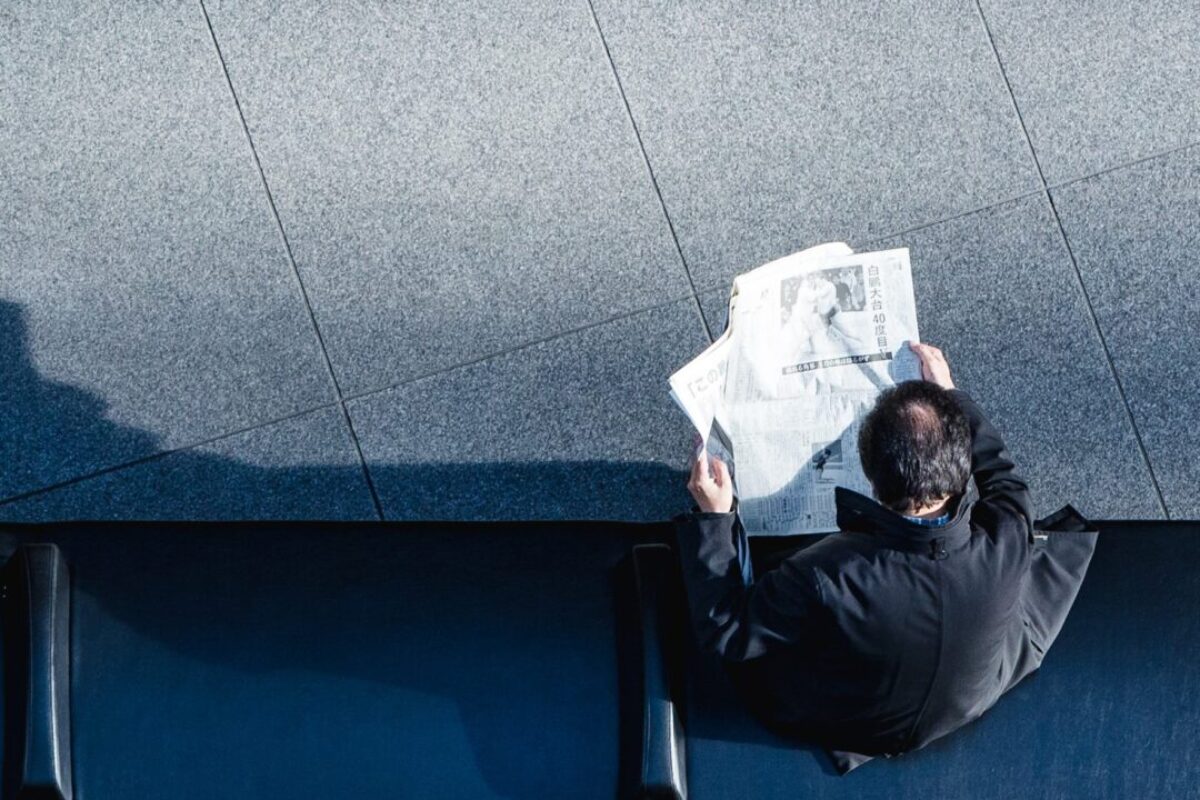 man reading newspaper on bench from above