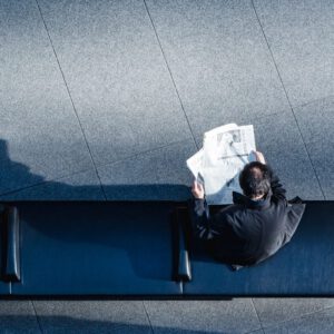 man reading newspaper on bench from above