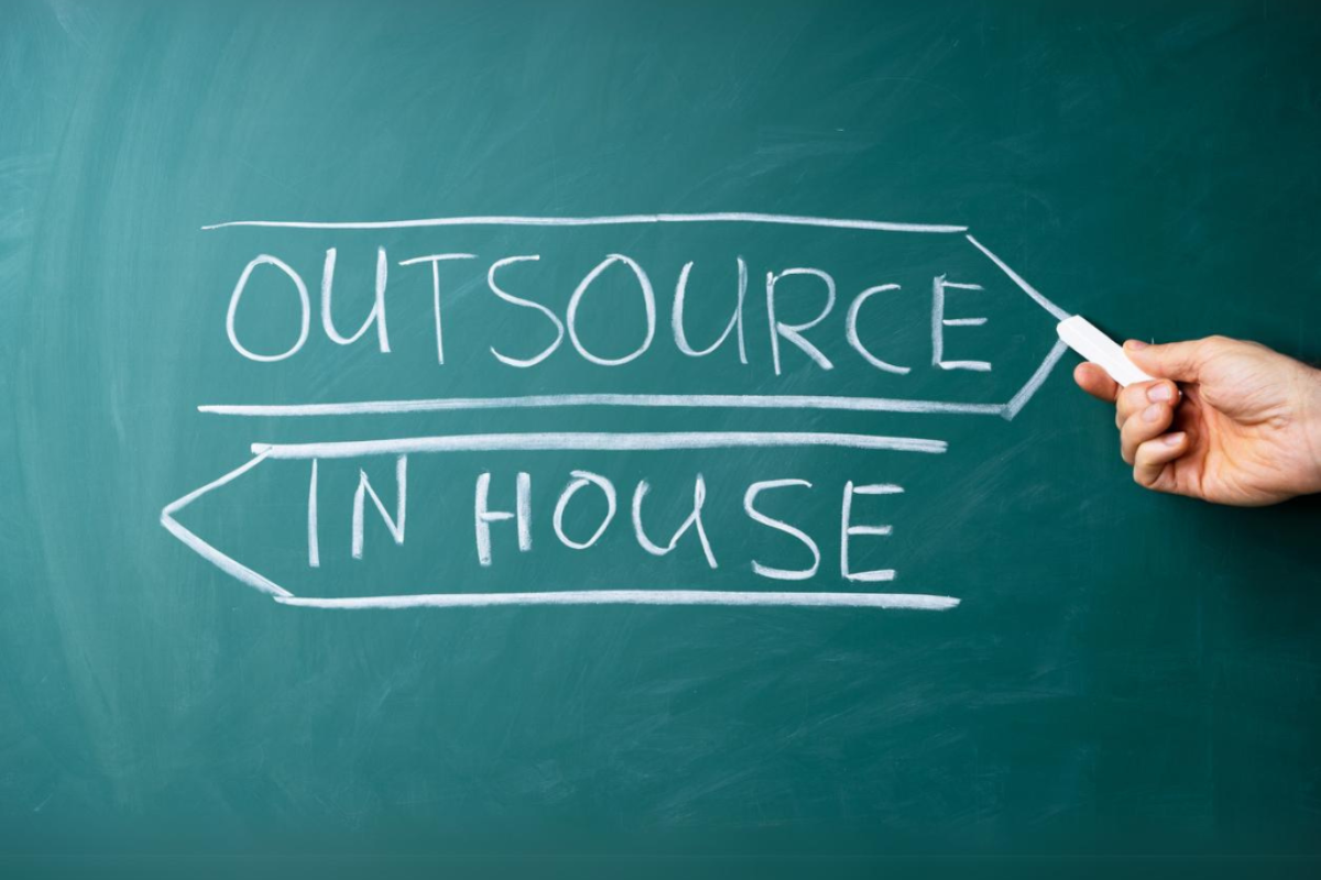 A blackboard with the words outsource and in house written in chalk