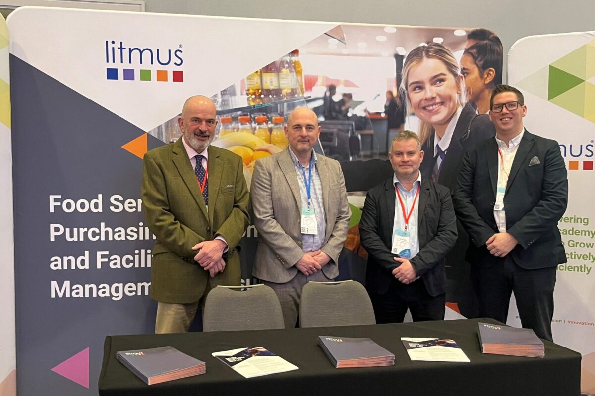 The Litmus team at the Confederation of School Trusts (CST) Finance and Operations Conference 2025. The team are stoofd in front of the Litmus stand. There are 4 of the team, all wearing suits.