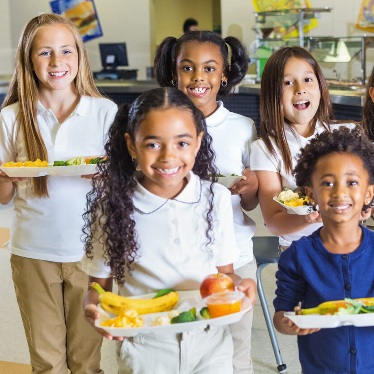 6 school children holding lunch trays filled with healthy food. The children are smiling and happy