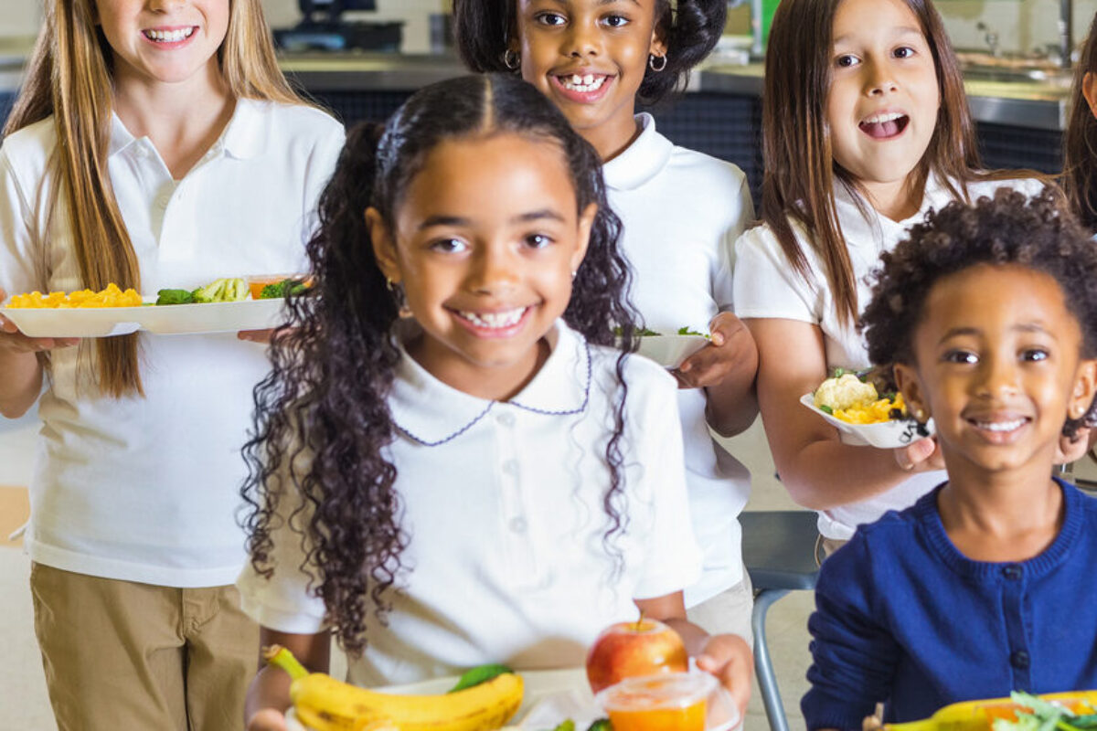 6 school children holding lunch trays filled with healthy food. The children are smiling and happy