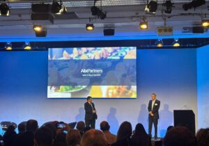 The stage at the Alix Partners event as seen from the audience. There are 2 presenters and a large screen