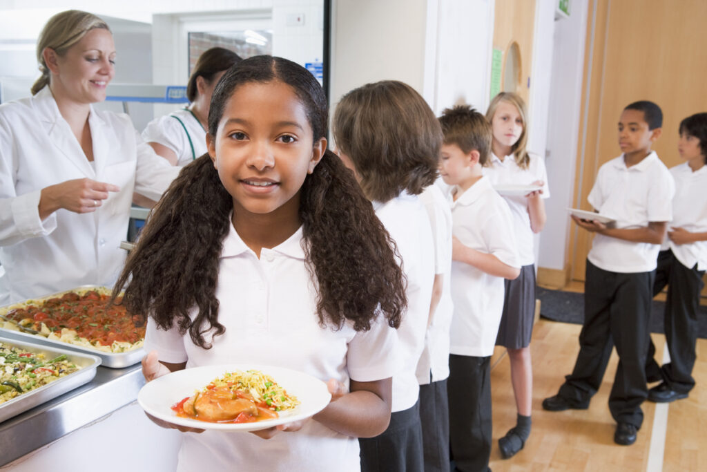 Children in white polo tops getting lunch in primary school